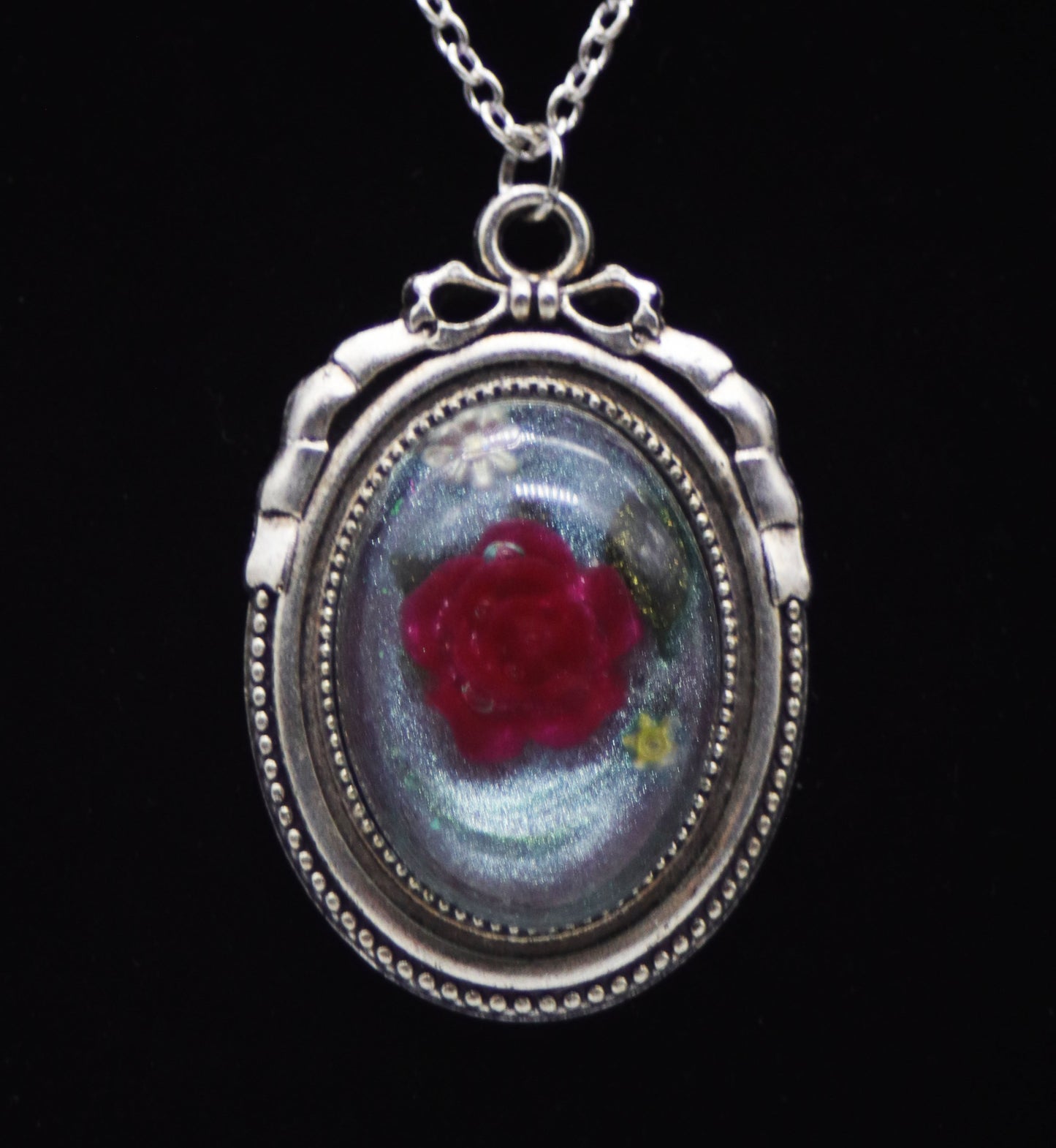 Deep red resin rose necklace with pressed leaves in silver-tone oval bow frame on silver chain against black background