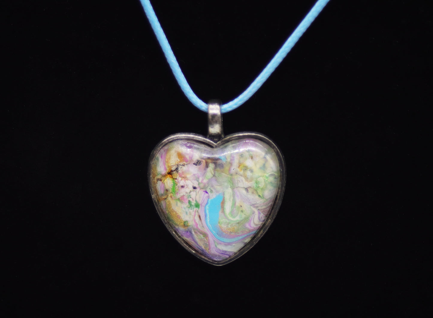 Pastel swirl paint skin glass cabochon heart necklace on light blue cord against black background