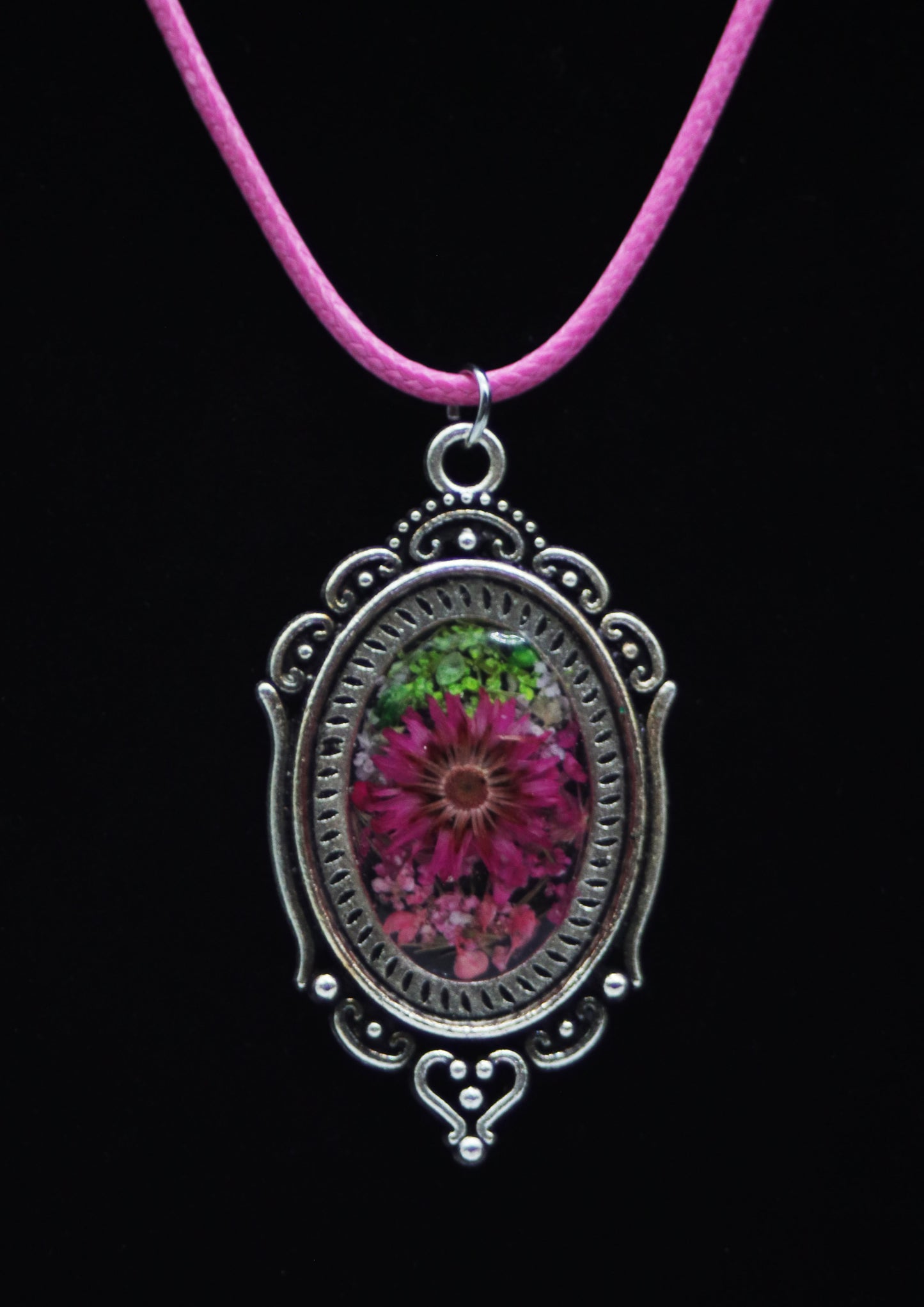 Victorian style magenta resin flower necklace in ornate silver-tone oval filigree frame on pink cord against black background