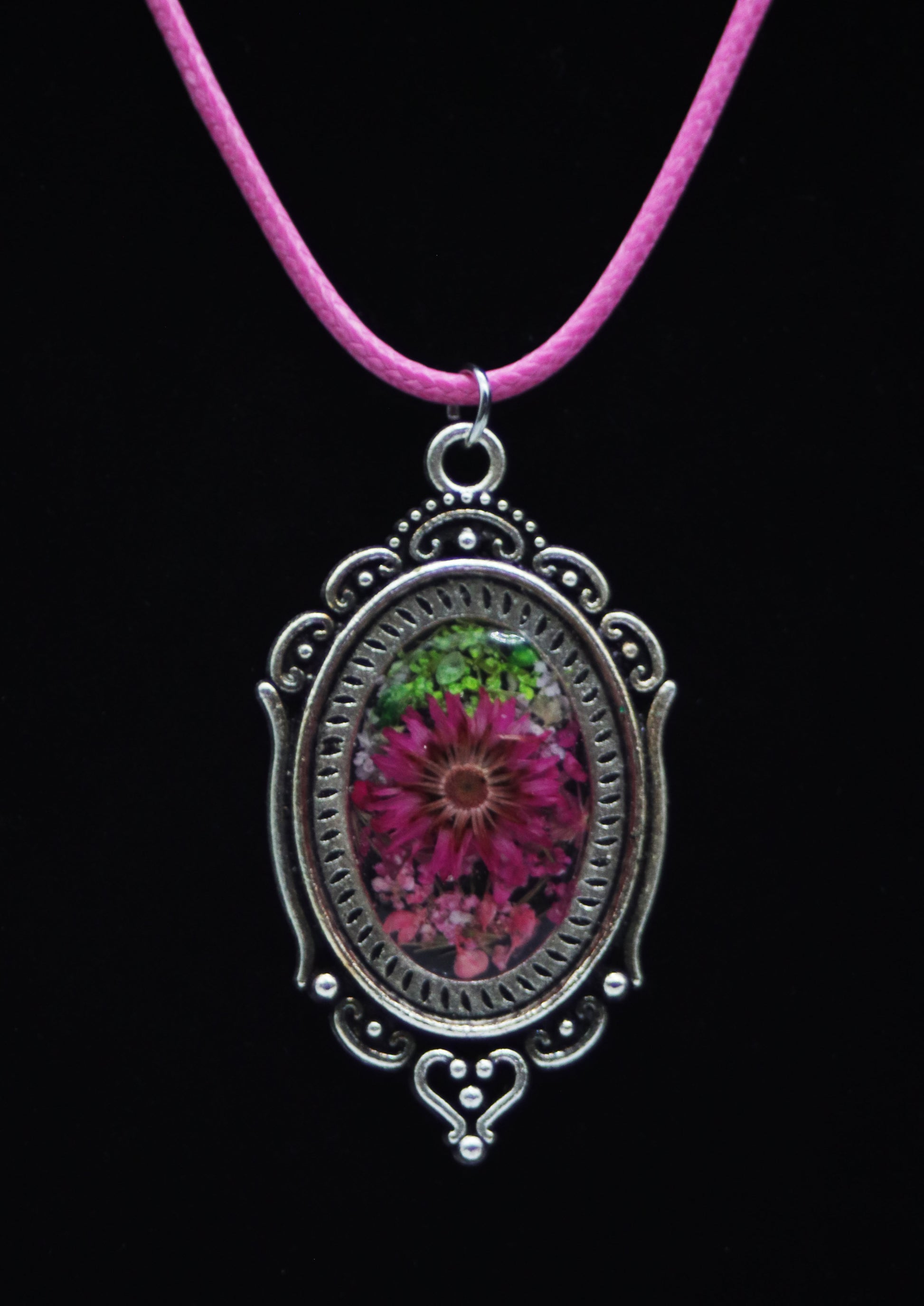 Victorian style magenta resin flower necklace in ornate silver-tone oval filigree frame on pink cord against black background