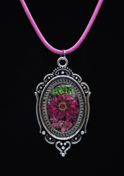 Victorian style magenta resin flower necklace in ornate silver-tone oval filigree frame on pink cord against black background