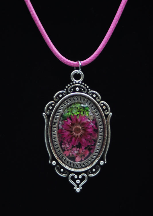 Victorian style magenta resin flower necklace in ornate silver-tone oval filigree frame on pink cord against black background