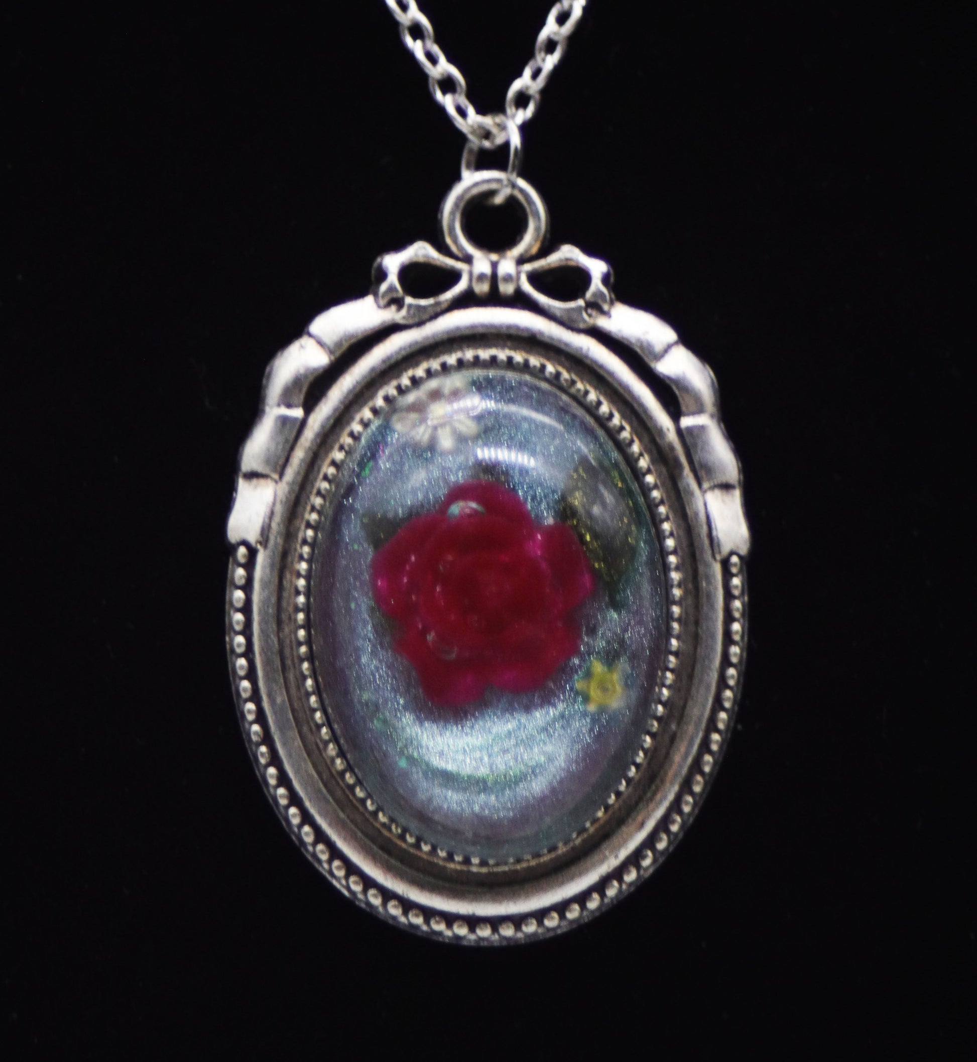 Deep red resin rose necklace with pressed leaves in silver-tone oval bow frame on silver chain against black background