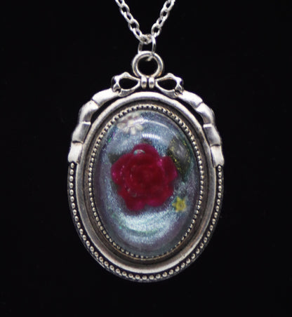 Deep red resin rose necklace with pressed leaves in silver-tone oval bow frame on silver chain against black background