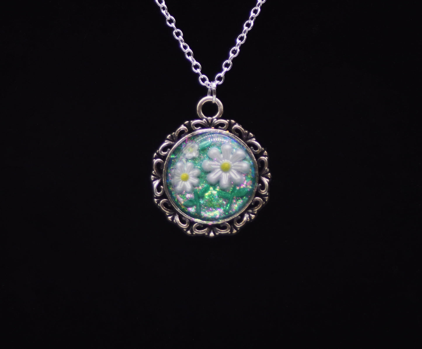 White resin daisy necklace with green glitter background in silver-tone round filigree frame on silver chain against black background