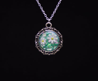 White resin daisy necklace with green glitter background in silver-tone round filigree frame on silver chain against black background