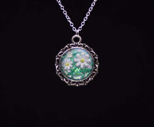 White resin daisy necklace with green glitter background in silver-tone round filigree frame on silver chain against black background