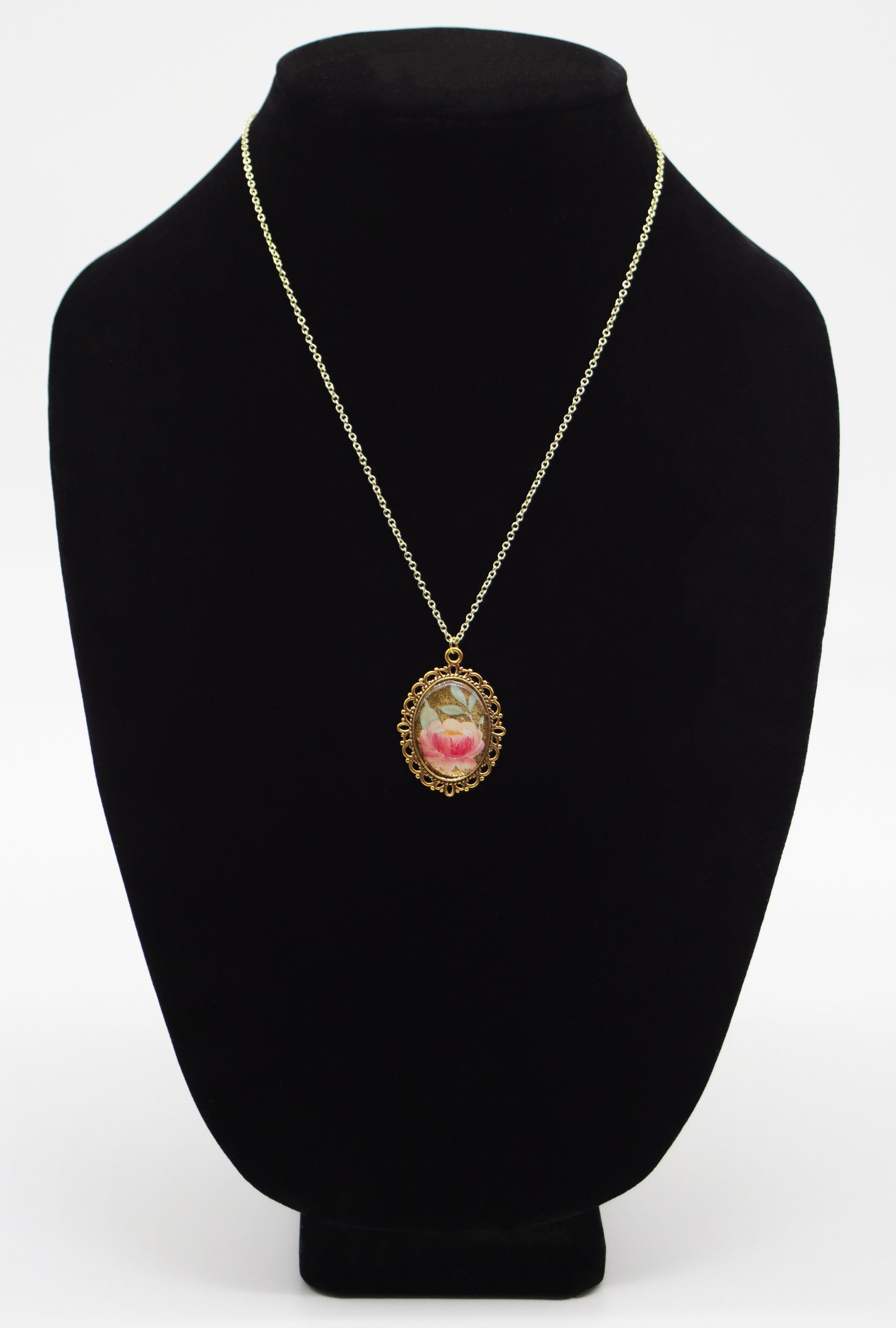 Pink rose mica resin necklace in gold-tone oval filigree frame on gold chain displayed on black jewelry bust