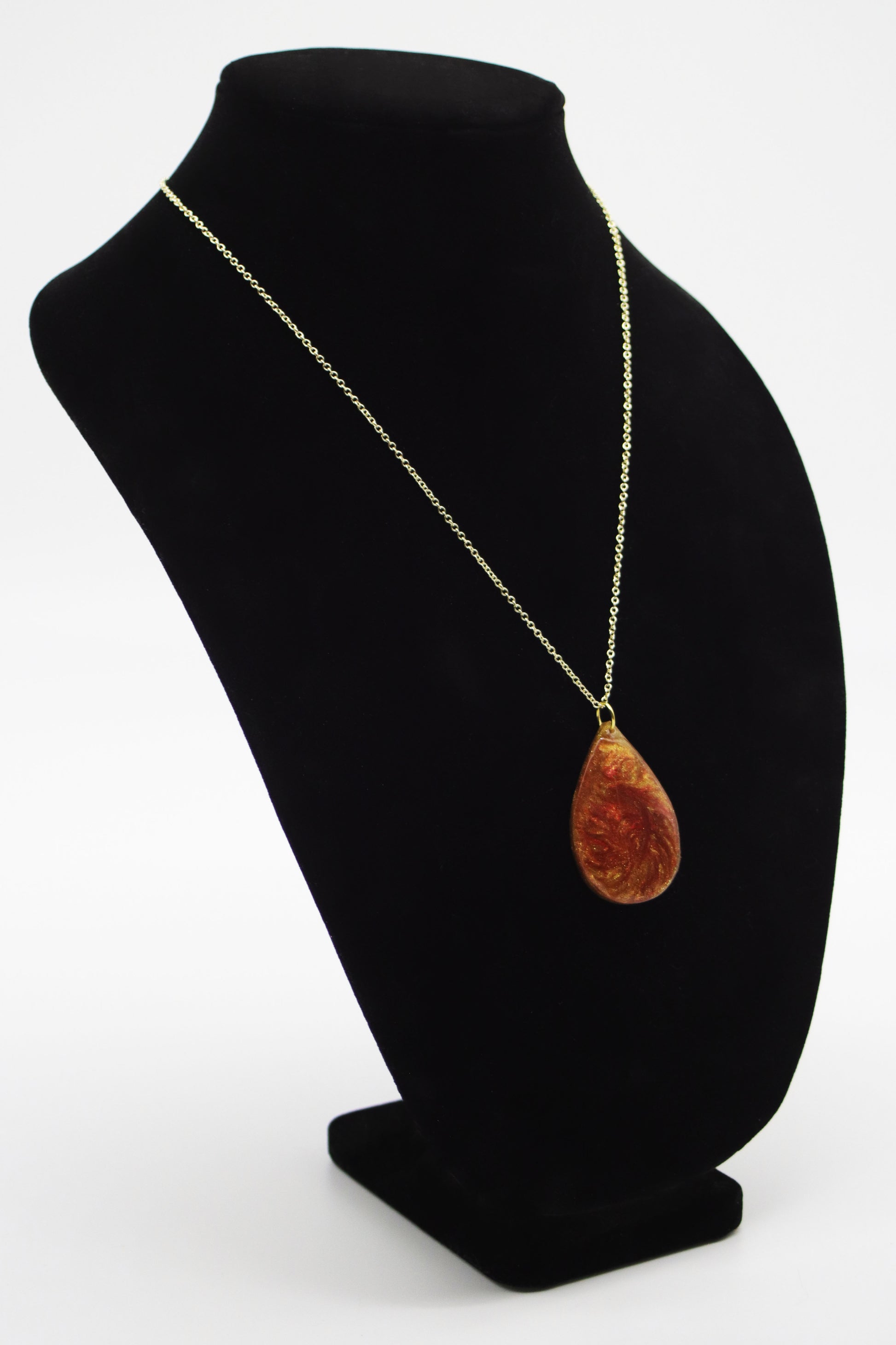 Amber and terracotta swirl resin teardrop necklace on gold-tone chain displayed on jewelry bust