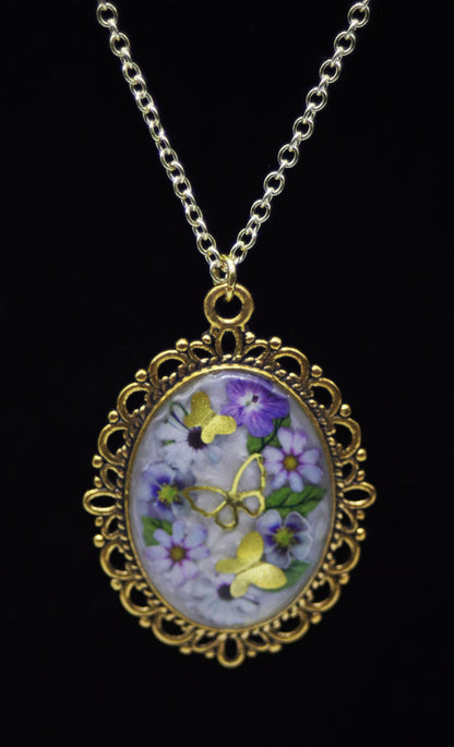 Gold oval domed resin necklace with purple pansies, lavender daisies, and gold butterfly accents