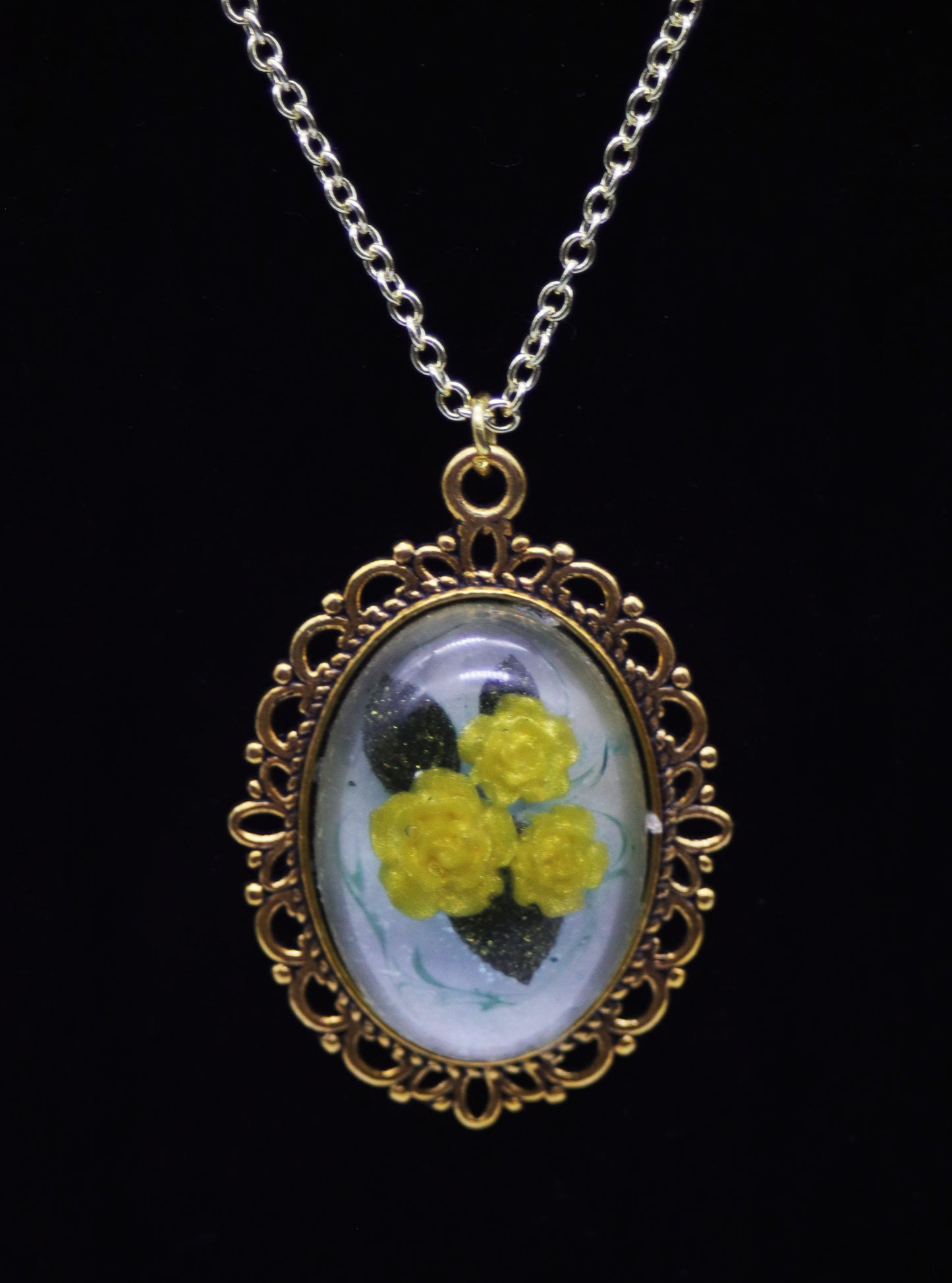 Gold oval resin necklace with three yellow resin roses and green leaves on pearlescent background