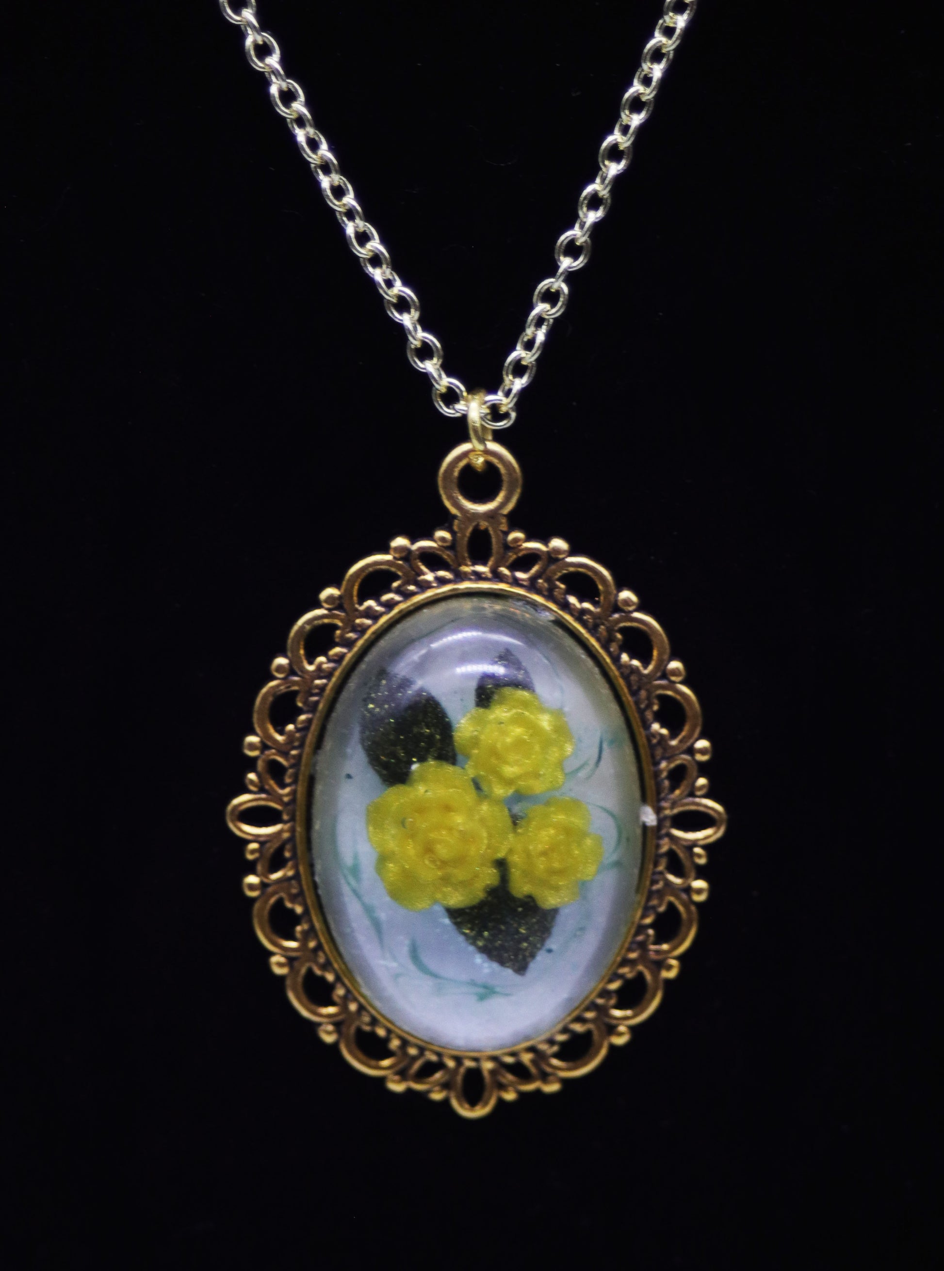 Gold oval resin necklace with three yellow resin roses and green leaves on pearlescent background