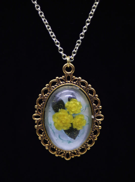 Gold oval resin necklace with three yellow resin roses and green leaves on pearlescent background