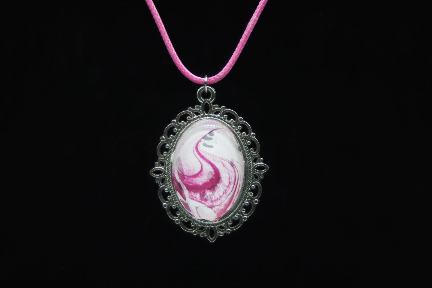 Silver filigree oval necklace with glass cabochon over hot pink and white swirl paint skin on pink cord