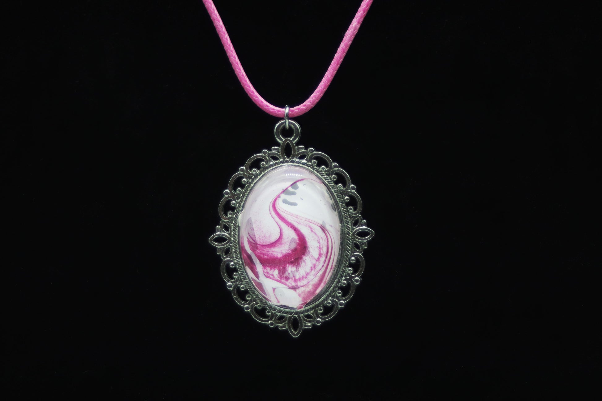 Silver filigree oval necklace with glass cabochon over hot pink and white swirl paint skin on pink cord