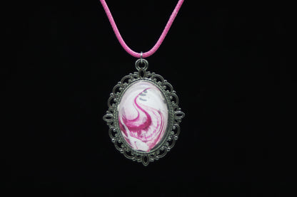 Silver filigree oval necklace with glass cabochon over hot pink and white swirl paint skin on pink cord