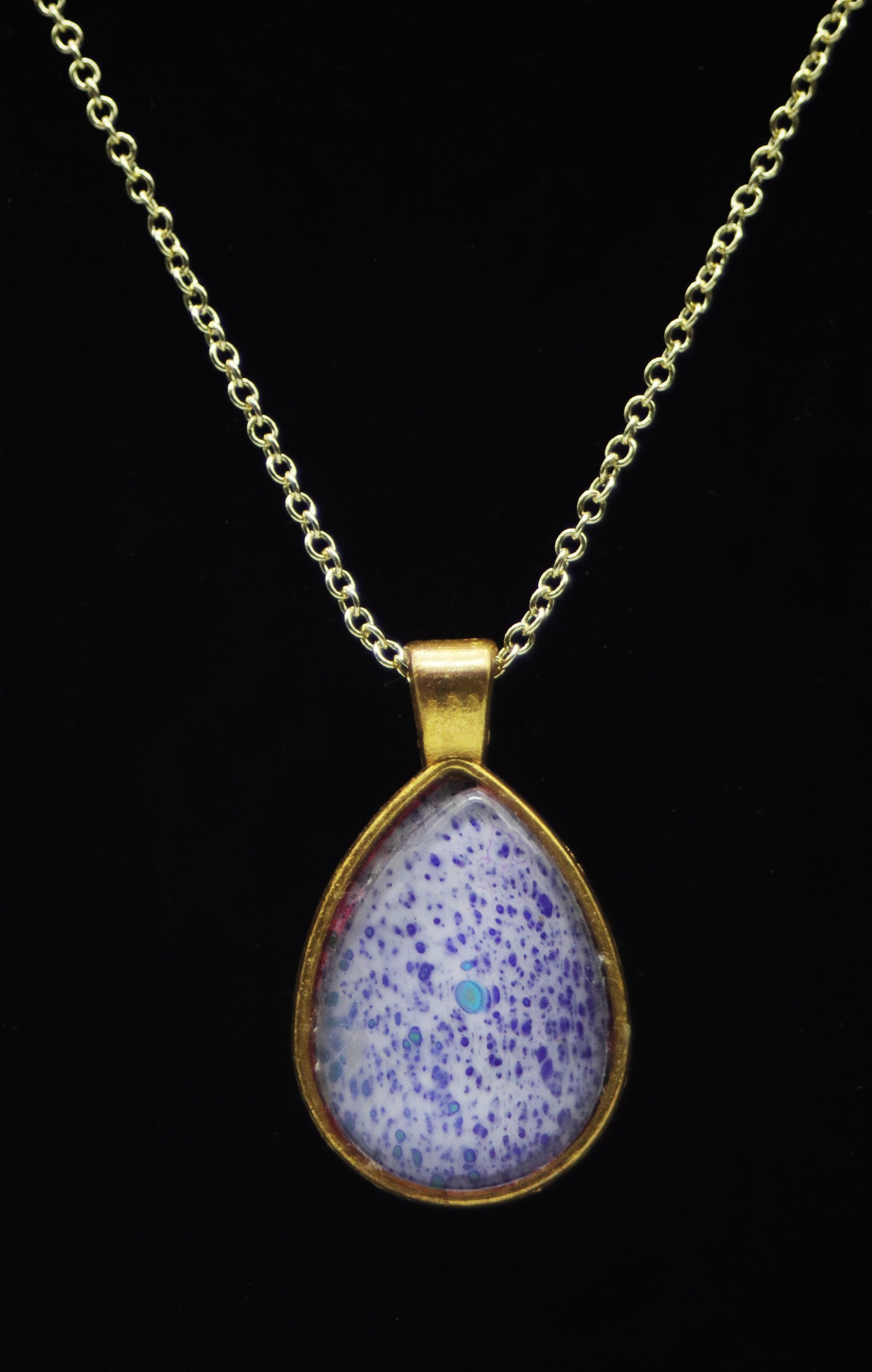 Gold teardrop necklace with glass cabochon over lavender periwinkle purple speckle paint skin